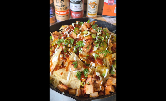Picture of finished grilled BBQ nachos in a cast iron pan with featured products behind it