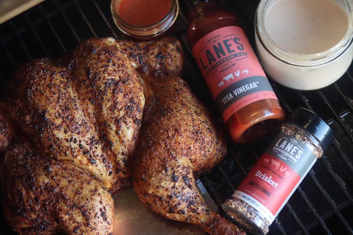 Lane's BBQ seasoning and sauce next to a rubbed spatchcock chicken on a grill