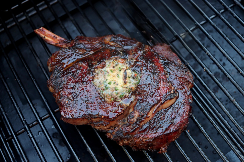Thick grilled steak sliced on a board beside a two-zone grill